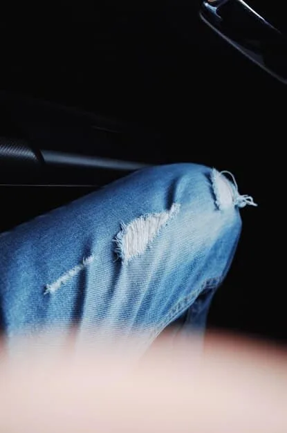 A close-up shot of a chic denim on denim outfit detail, showing a light wash denim jacket layered over a dark denim shirt, with layered gold chain necklaces peeking through, and a slim leather belt cinching the waist.