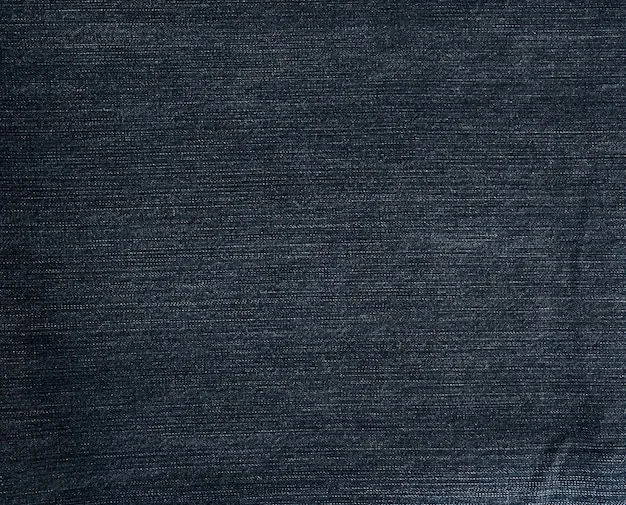A close-up shot of raw, dark indigo denim fabric, highlighting its rich texture and deep color, with subtle stitching details visible.