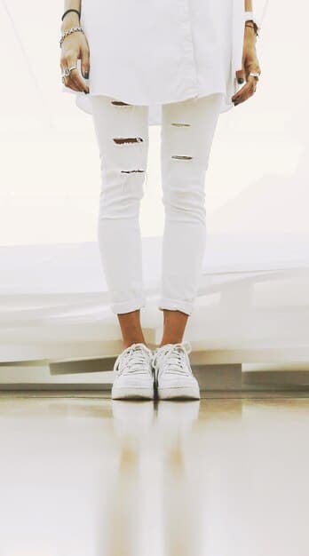 A close-up shot of a pair of clean white minimalist sneakers paired with tailored trousers, showcasing how simple footwear can elevate a casual-chic look. The background is a clean, modern floor.