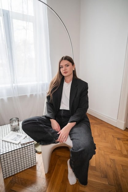 A person wearing a soft knit blazer in a neutral color over a simple silk top, paired with comfortable yet tailored dark wide-leg trousers, sitting in a stylish home office.