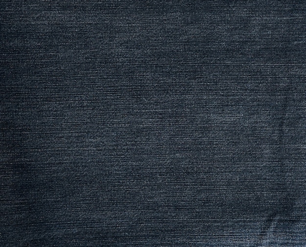 A close-up shot of raw, dark indigo denim fabric, highlighting its rich texture and deep color, with subtle stitching details visible.