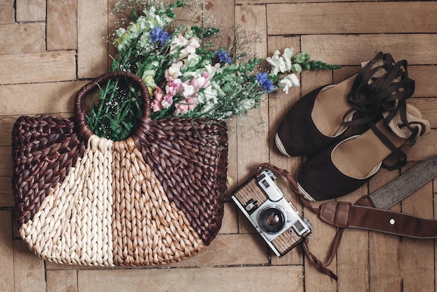 A flat lay of cottagecore accessories: a straw hat, a woven basket bag, a pair of leather sandals, and a small wildflower bouquet.